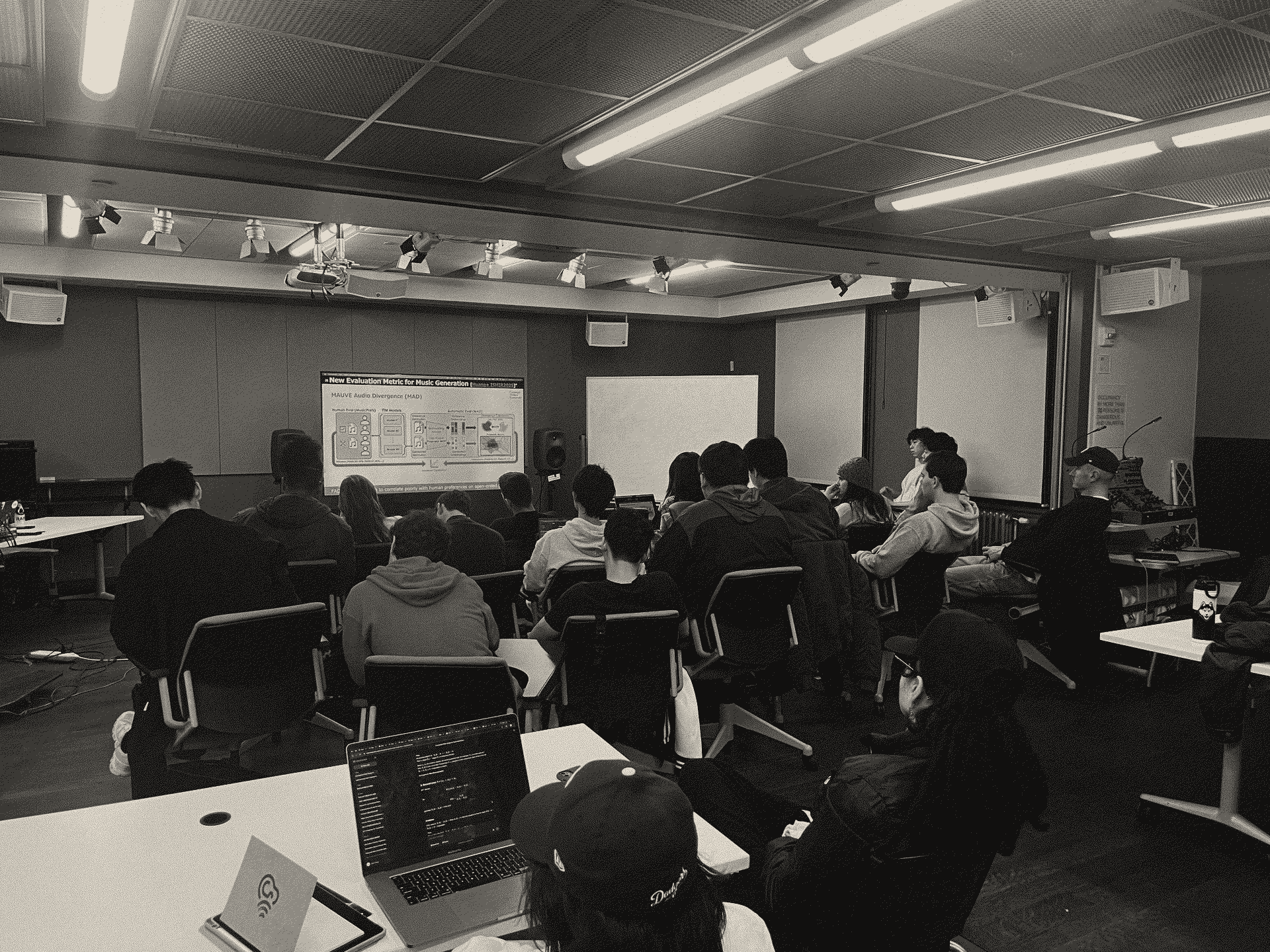 Members at a general meeting, watching a talk on music generation